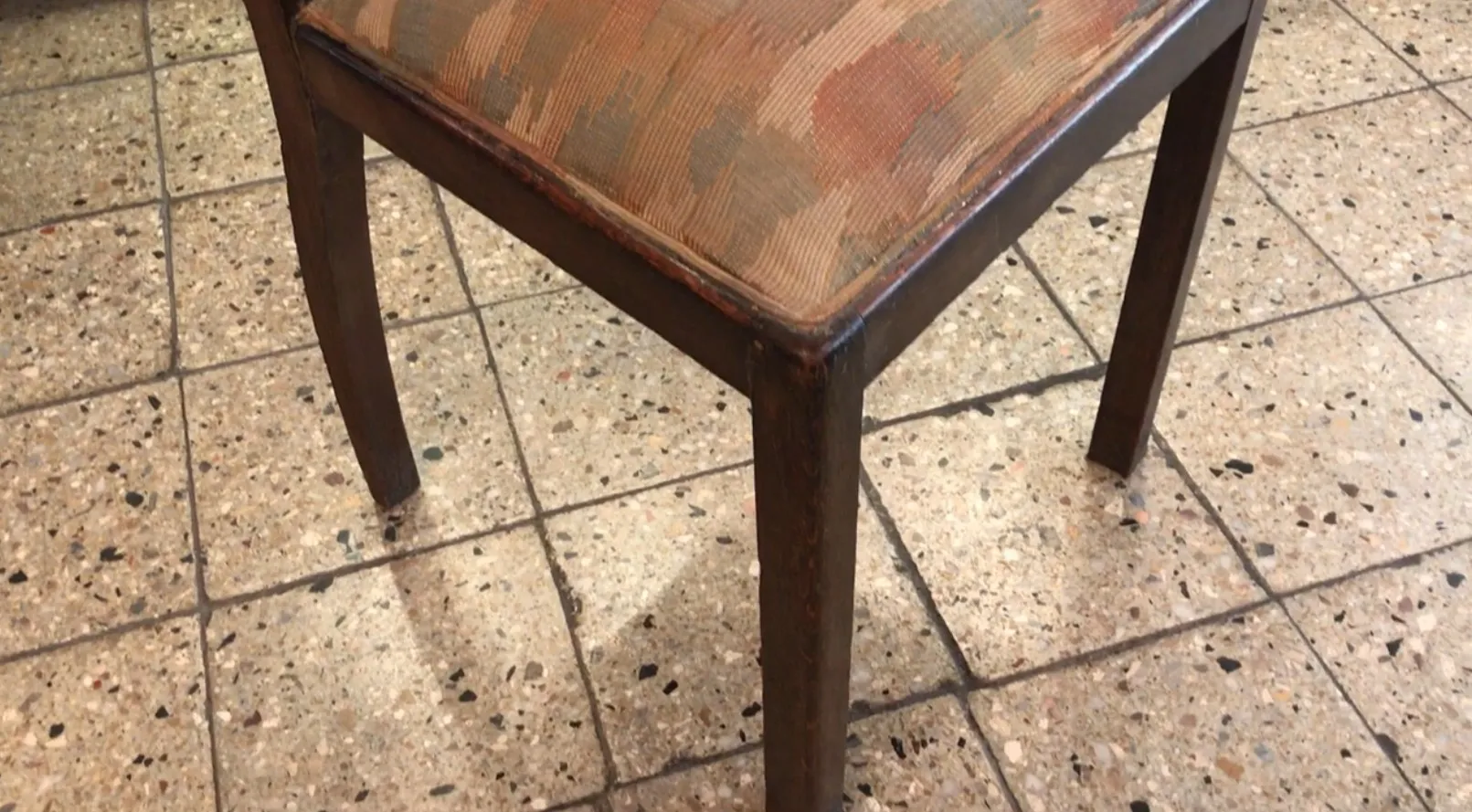 antique art deco chair with upholstery in brown and ochre hues, placed on tiled floor