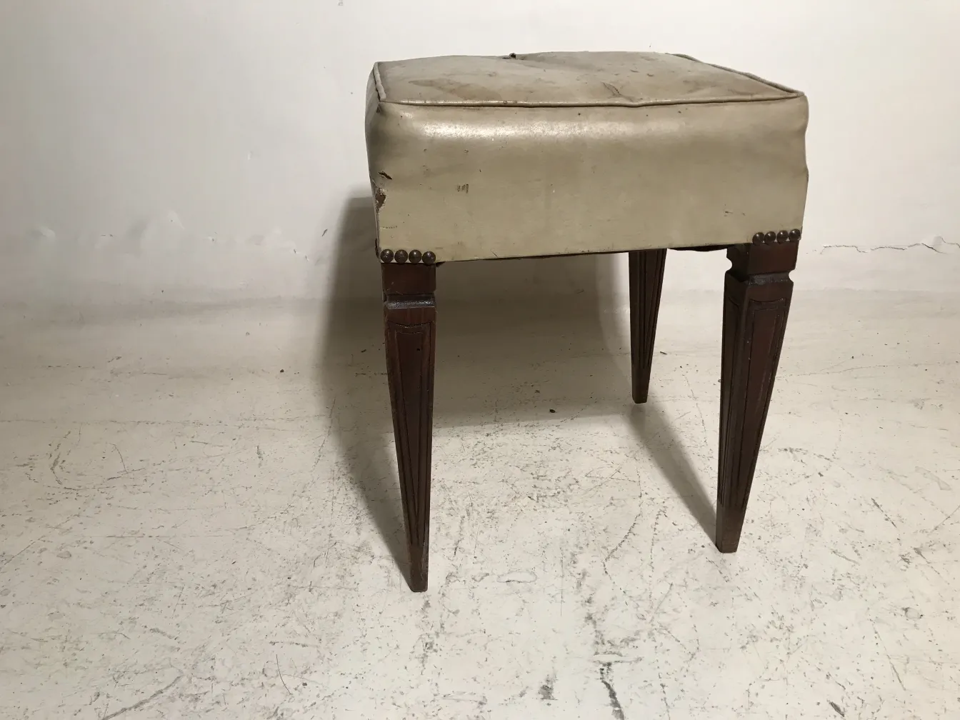tabouret ancien avec jambes décorées, fond neutre.