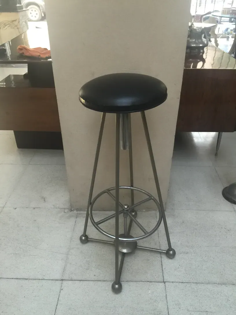 Tabouret ancien avec assise noire et base à roue dans un cadre moderne.
