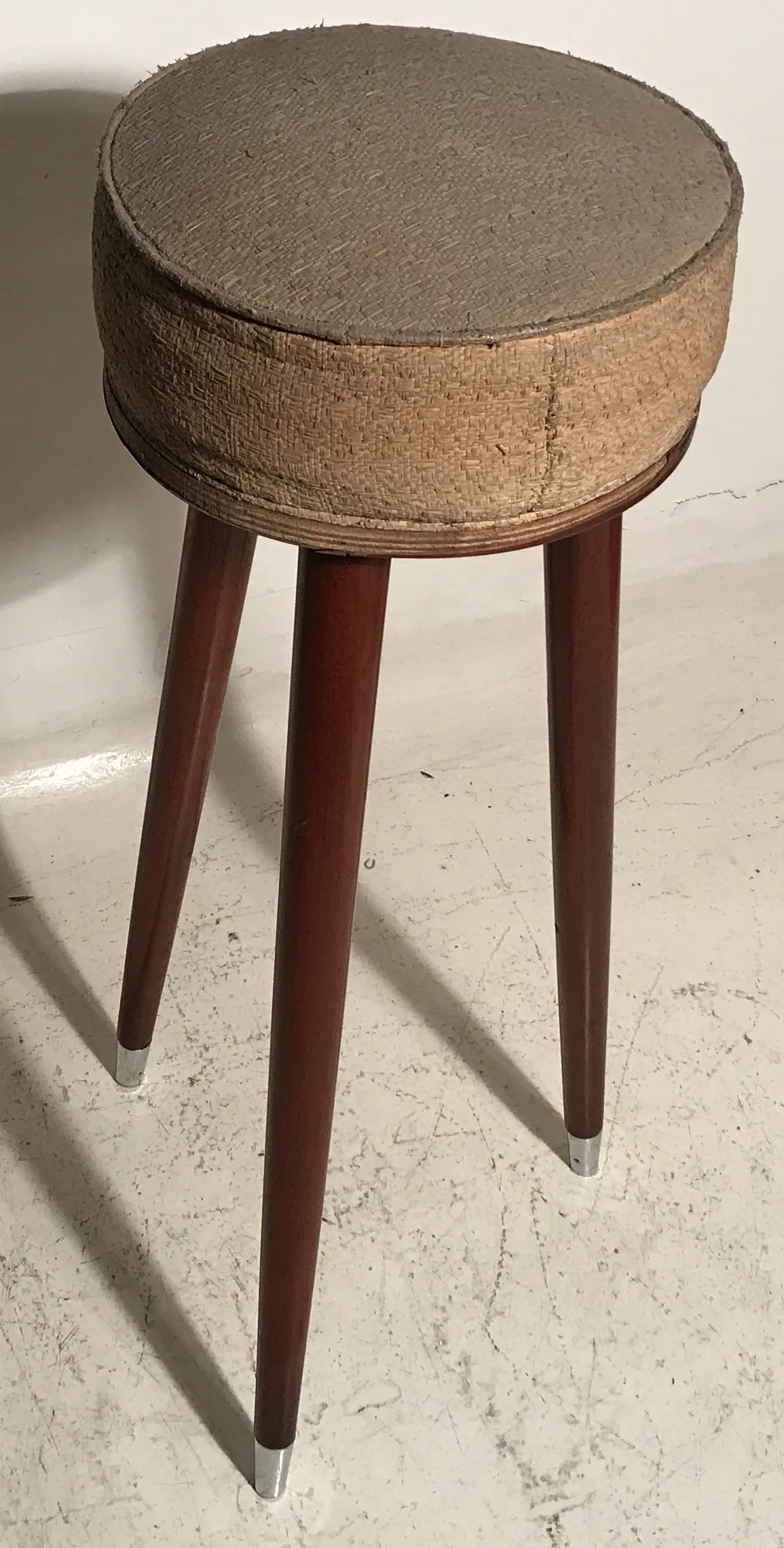 Antique stool with long legs, round design in brown color, set against a neutral background.