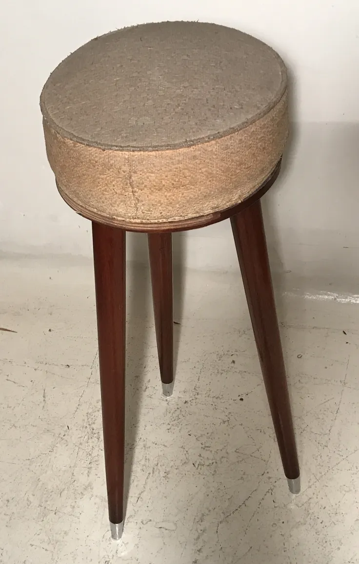 antique stool with a round shape and tall legs in a neutral setting