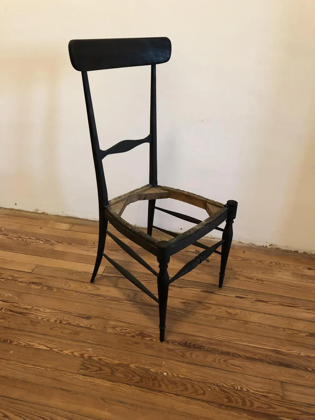 Old wooden chair with backrest, missing seat, in a light wood setting.