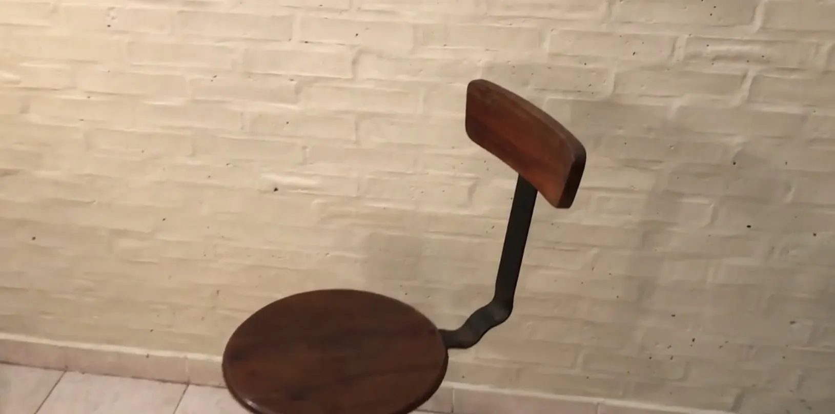 Sgabello antico marrone con schienale, in un ambiente neutro.