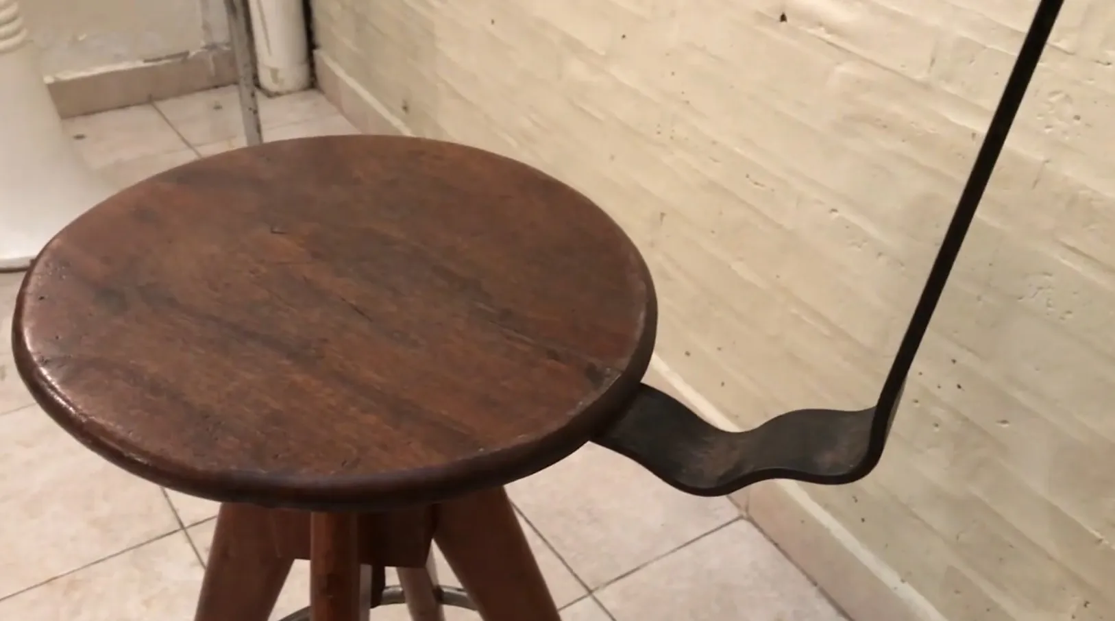 Banqueta antigua con asiento redondo y patas de madera.