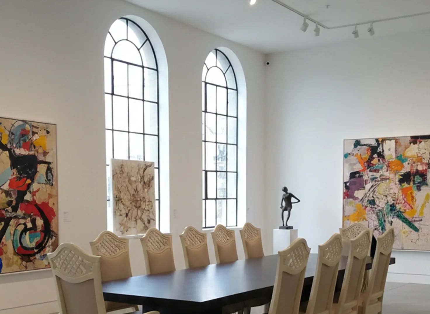 Vista de 12 sillas antiguas dispuestas en una mesa amplia dentro de una sala luminosa con arte contemporáneo