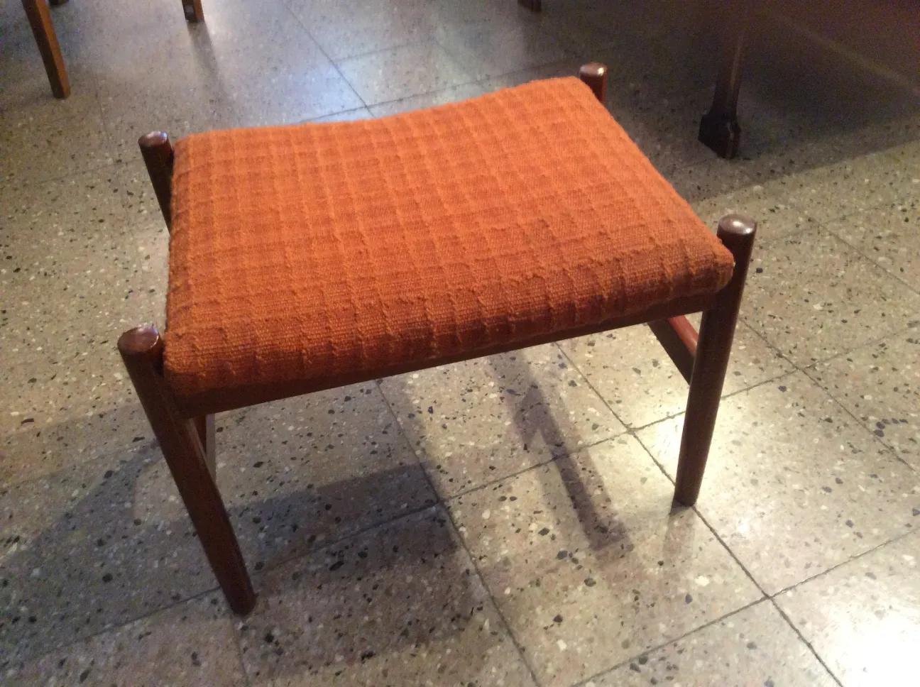 Antigua banqueta con asiento tapizado en color naranja, en un ambiente retro.