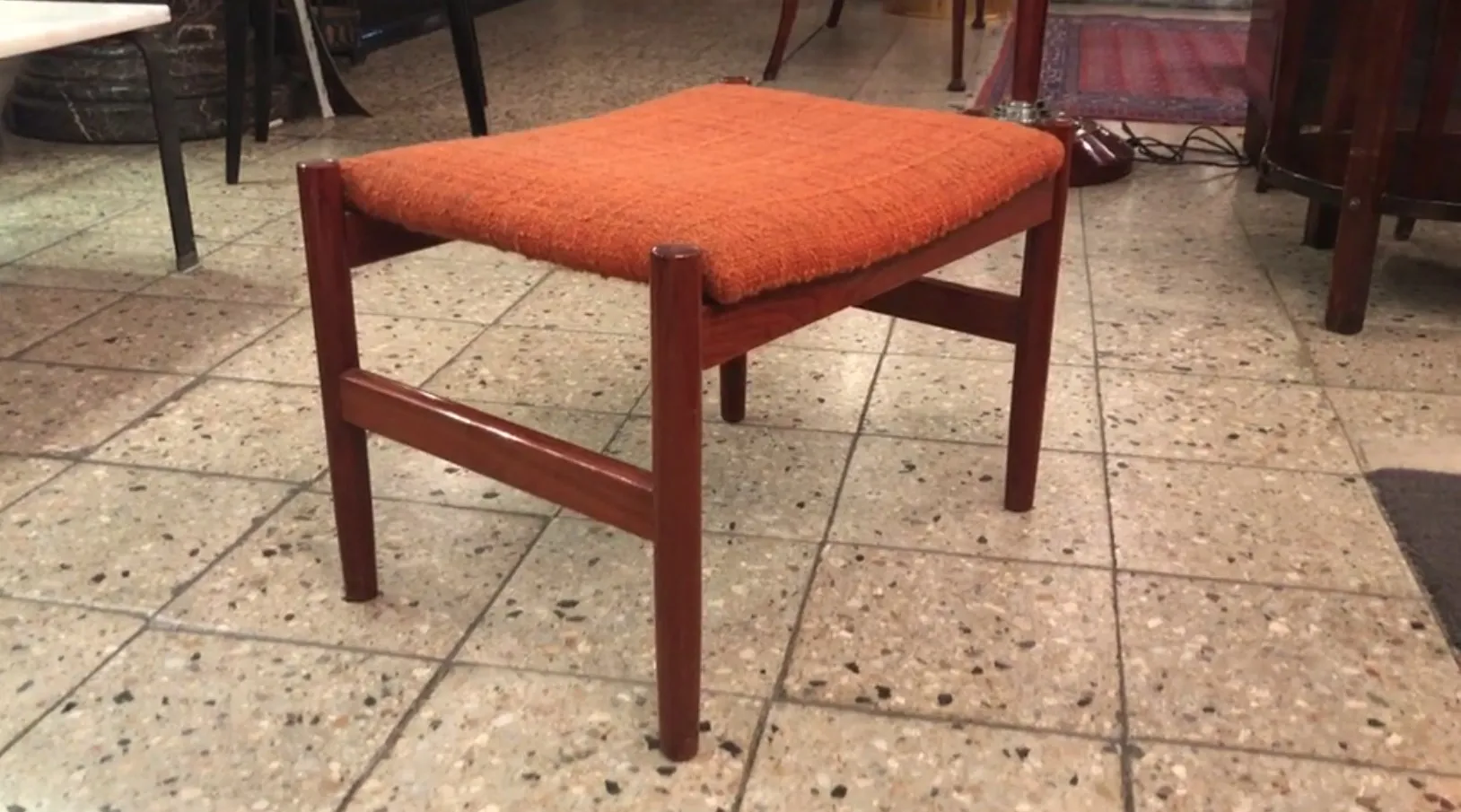 Antiker Hocker mit leuchtend orangefarbigem Kissen