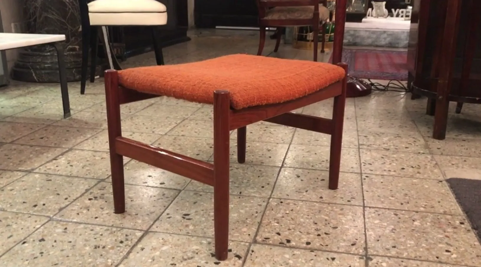 Tabouret ancien orange avec des pieds en bois dans un cadre accueillant.