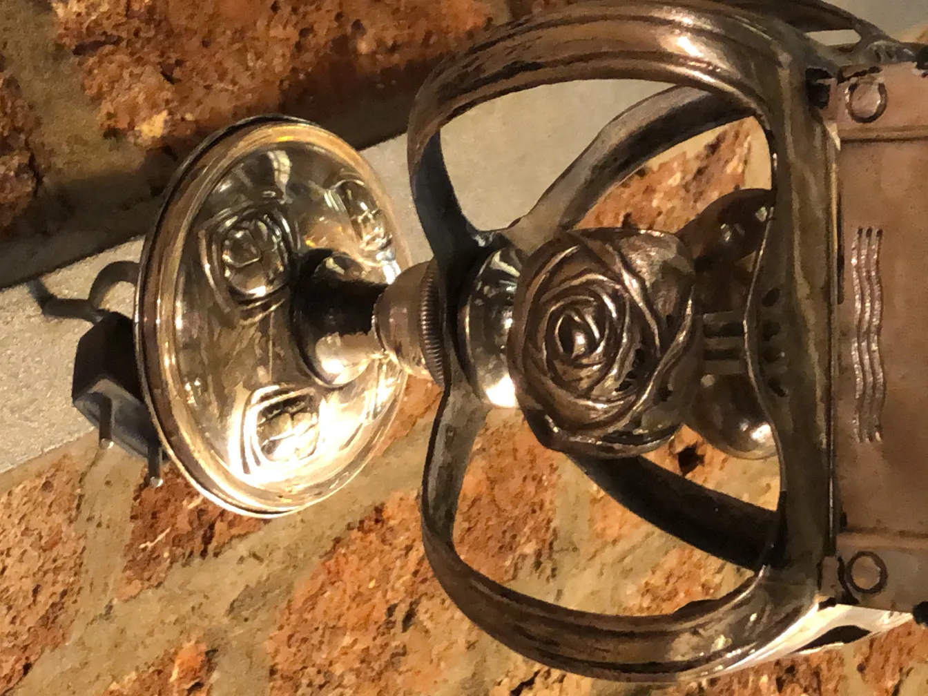 antike Metalllampe mit Rosendekor vor einer Ziegelwand