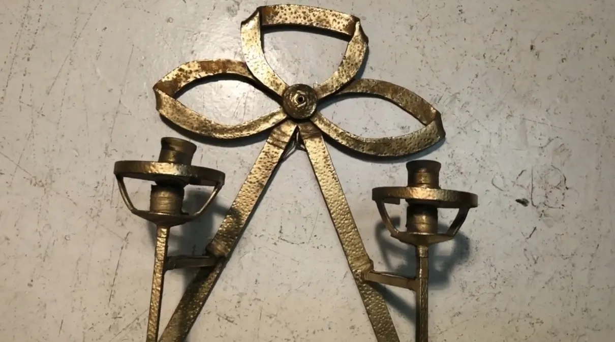 Apliques antiguos con forma de lazo, iluminando suavemente una pared blanca, creando un ambiente acogedor.