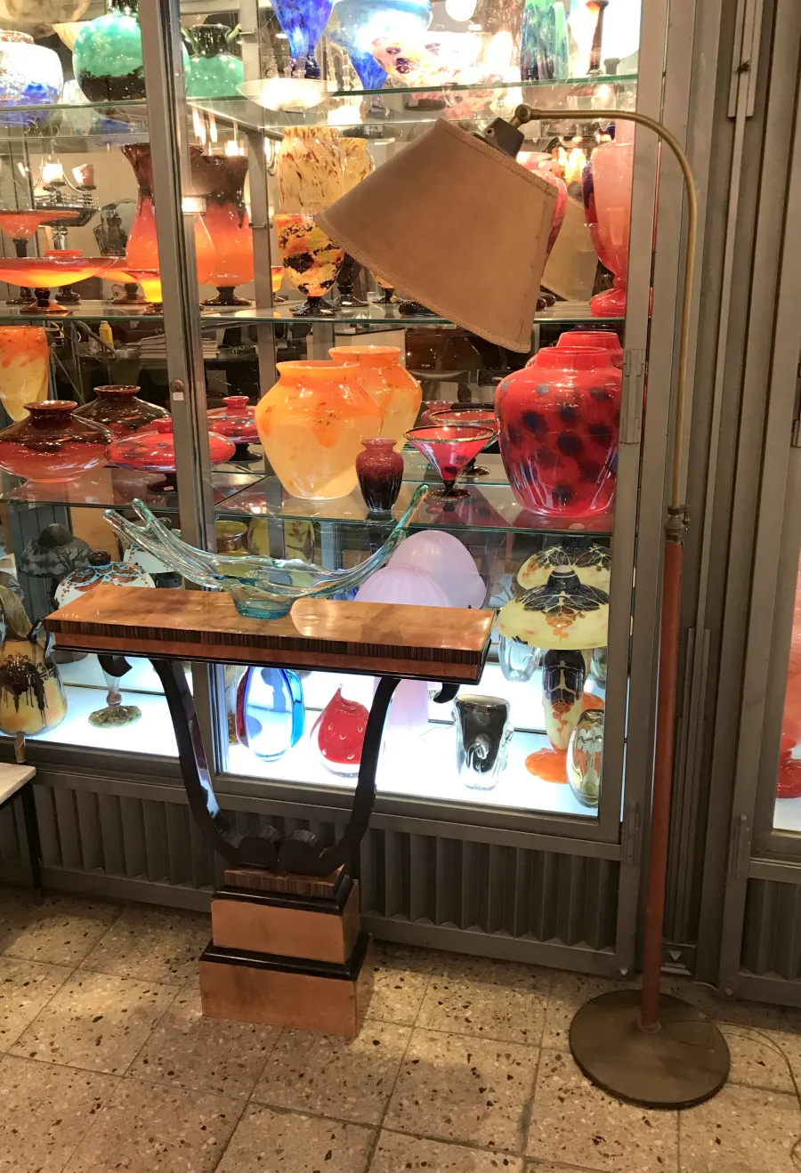 antique floor lamp with a beige shade and decorative base surrounded by colorful glass vases