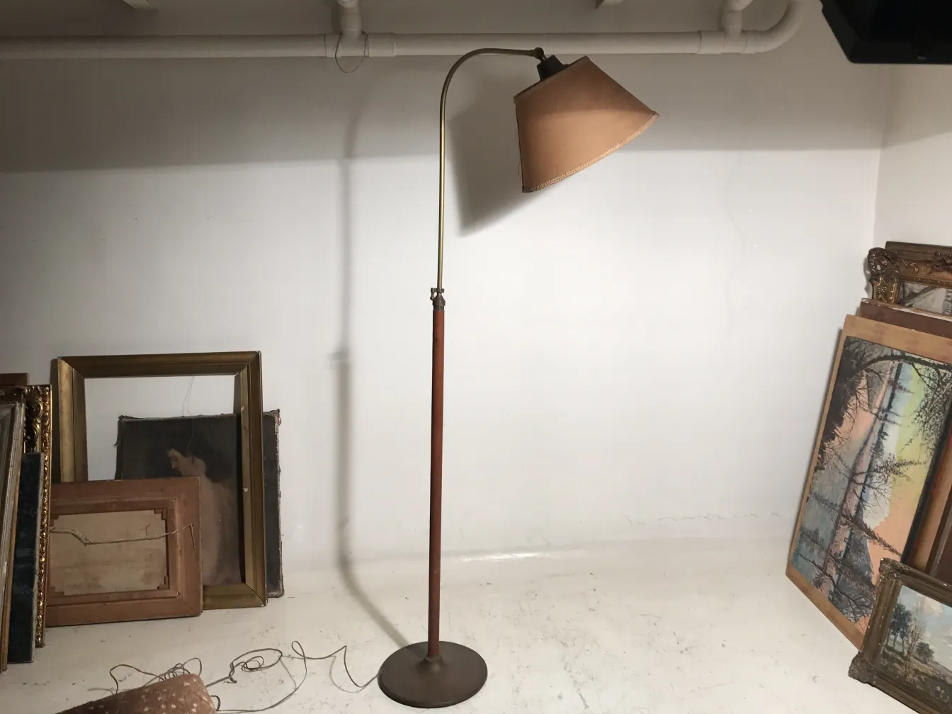 Lampada da terra antica con base rotonda e paralume marrone, sfondo bianco con cornici antiche.