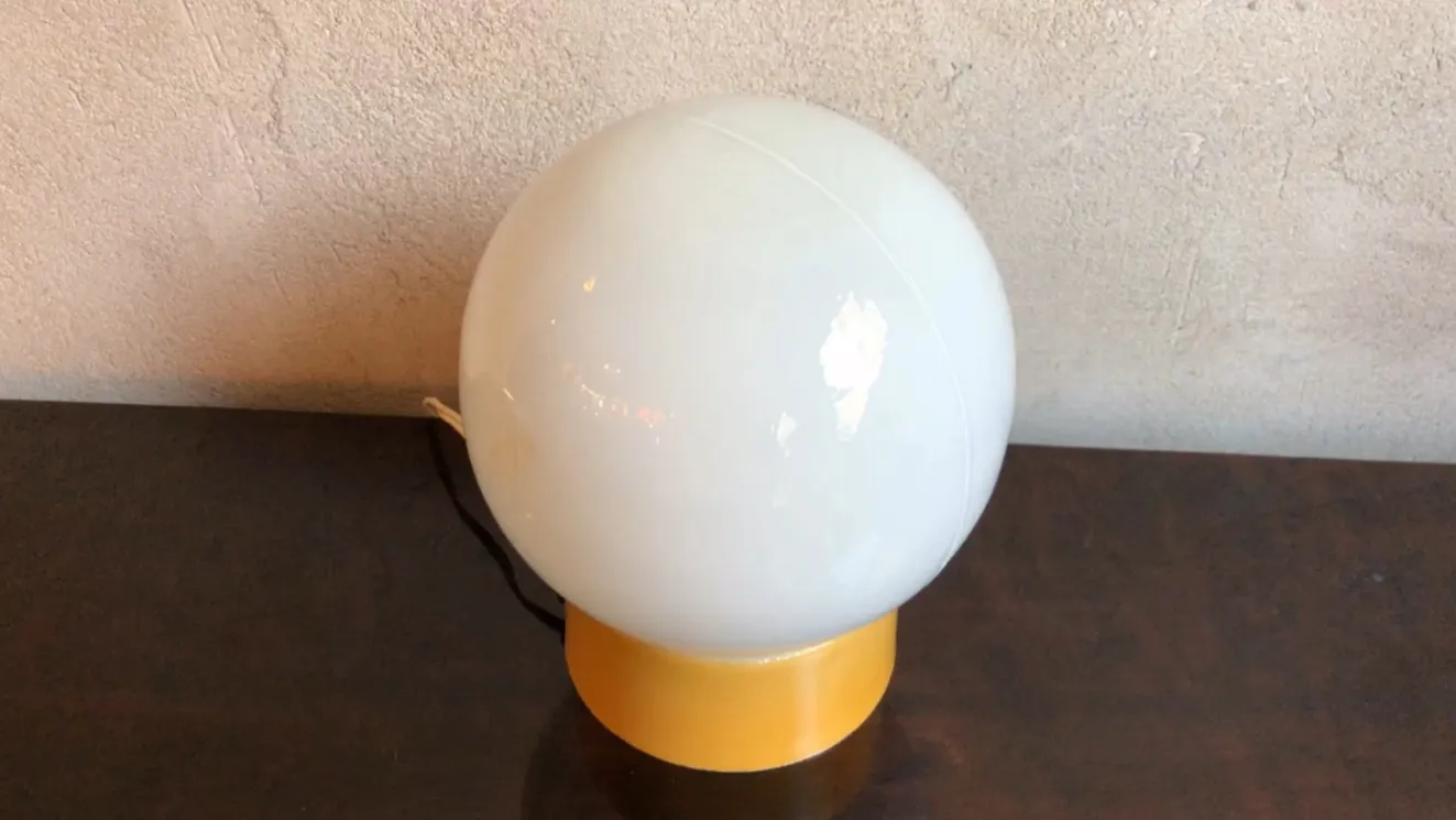 Luminária de mesa antiga esférica sobre uma mesa escura, com fundo claro.