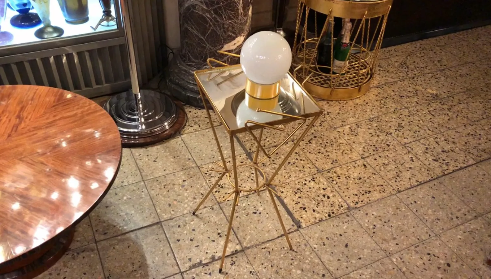 Antique table lamp with gold base and white sphere, enhancing an elegant setting. Tables and decorative items in the background.