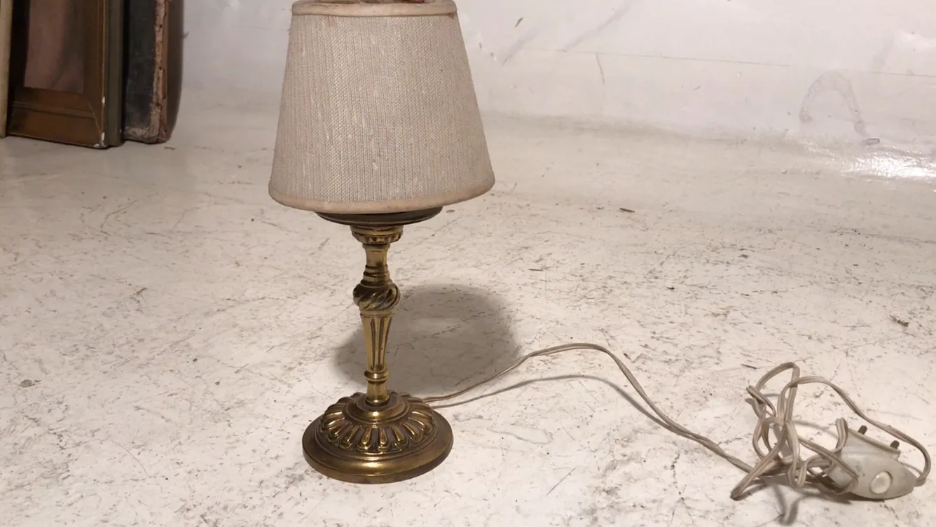table lamp with a gold base and light shade in an antique setting