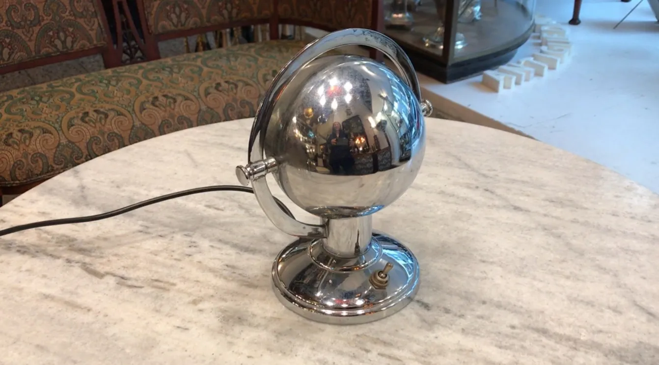 Lámpara de mesa antigua con base redonda y esfera brillante, estilo Art Deco, en un ambiente clásico.