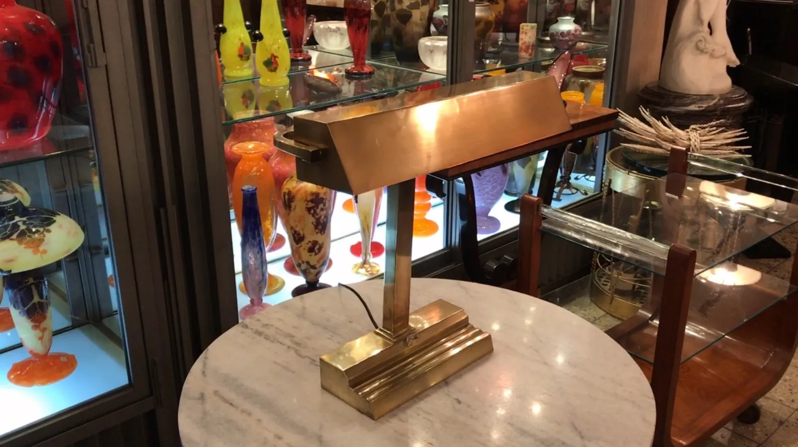 antike Tischlampe mit Art Deco-Design, umgeben von bunten Glasobjekten