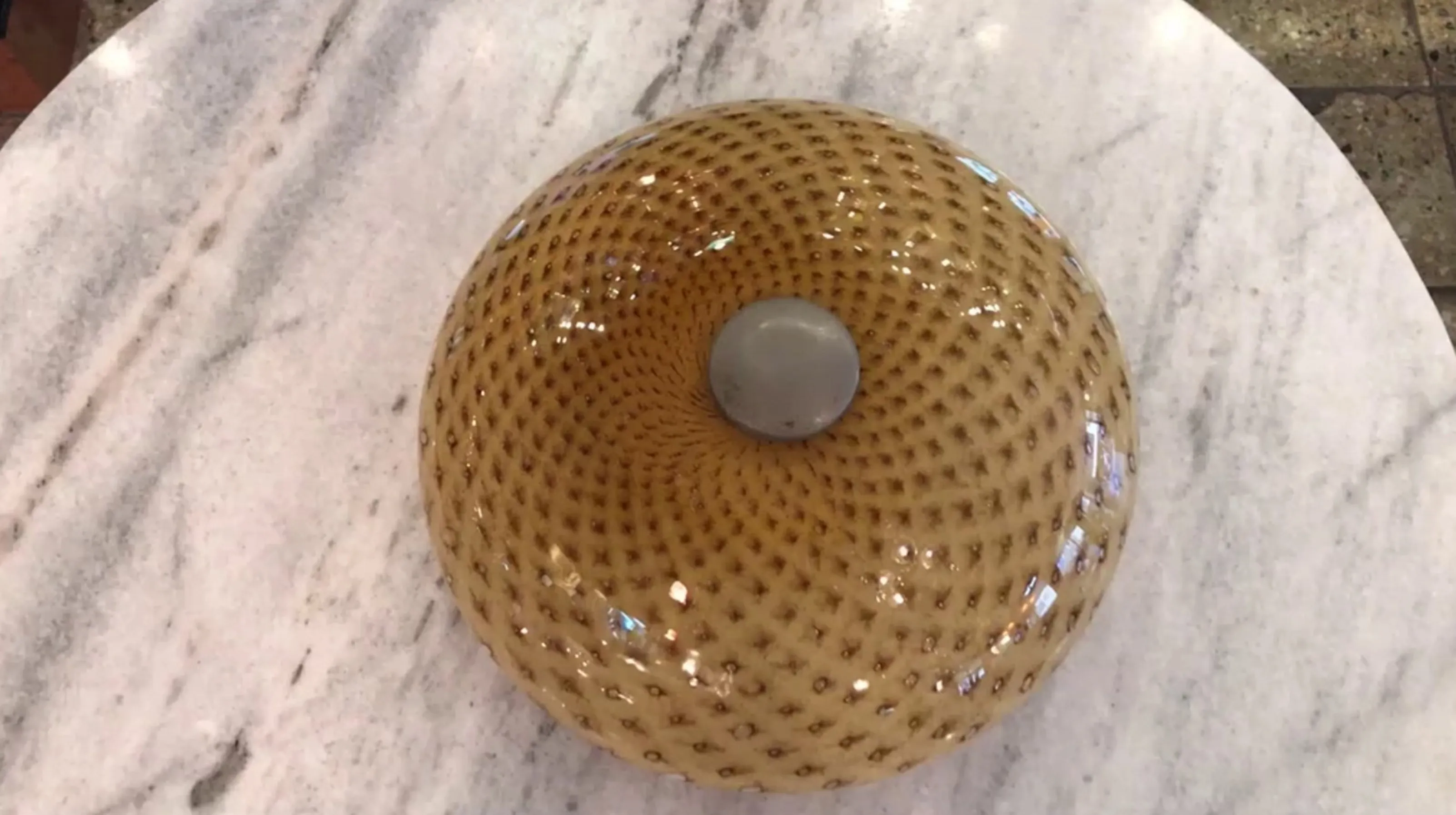 Plafonnier ancien de forme sphérique et de design texturé dans des tons chauds, décorant une surface brillante.