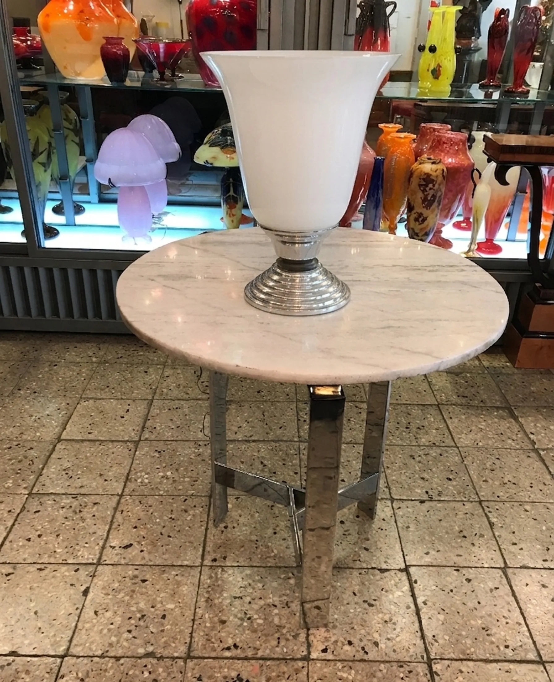 Antique table lamp with shiny metal base and white shade, set in an elegant decor with other decorative items.