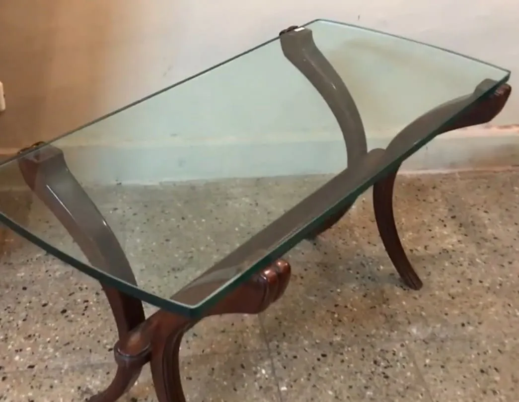 Table basse ancienne avec un plateau en verre et des pieds décoratifs, dans un cadre accueillant.