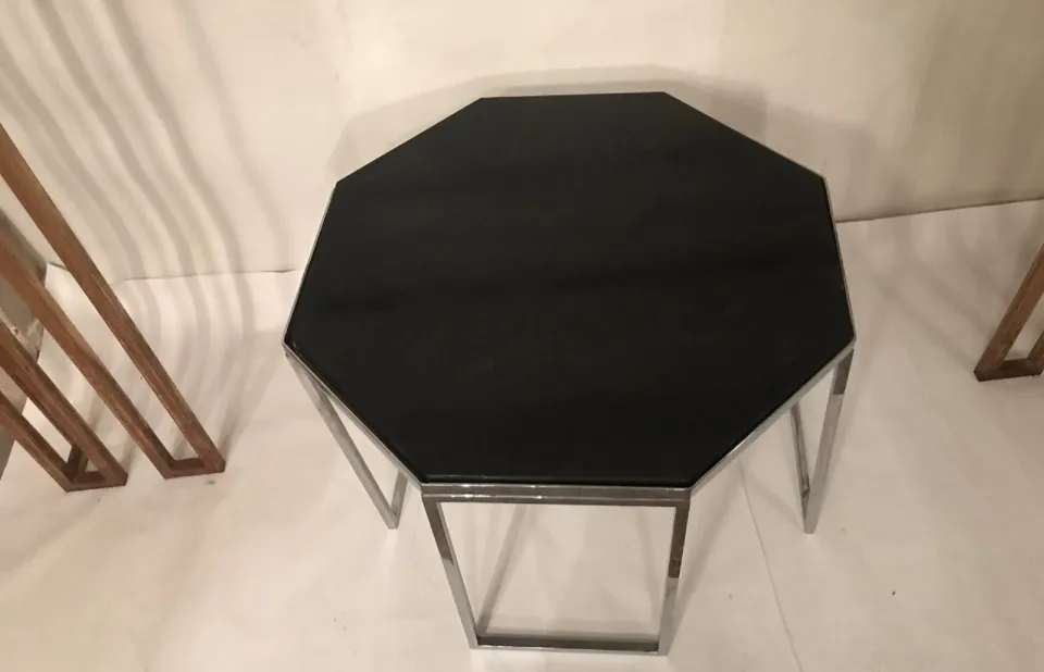 Mesa de centro octogonal com base metálica, antiga, em um ambiente minimalista.