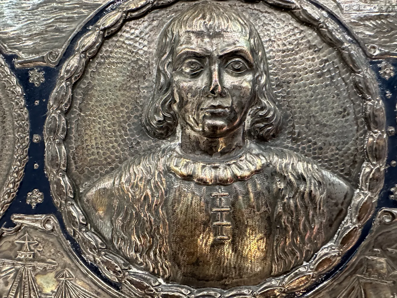 Placa de pared antigua con retrato de Cristóbal Colón en un entorno decorativo.