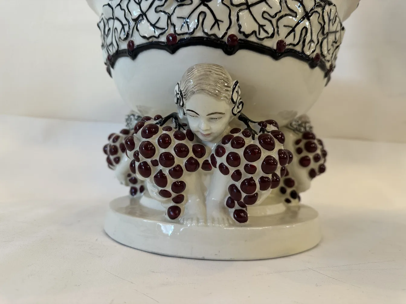 Antigua cerámica con figuras de personas y uvas decorativas, exhibiendo un bello diseño.