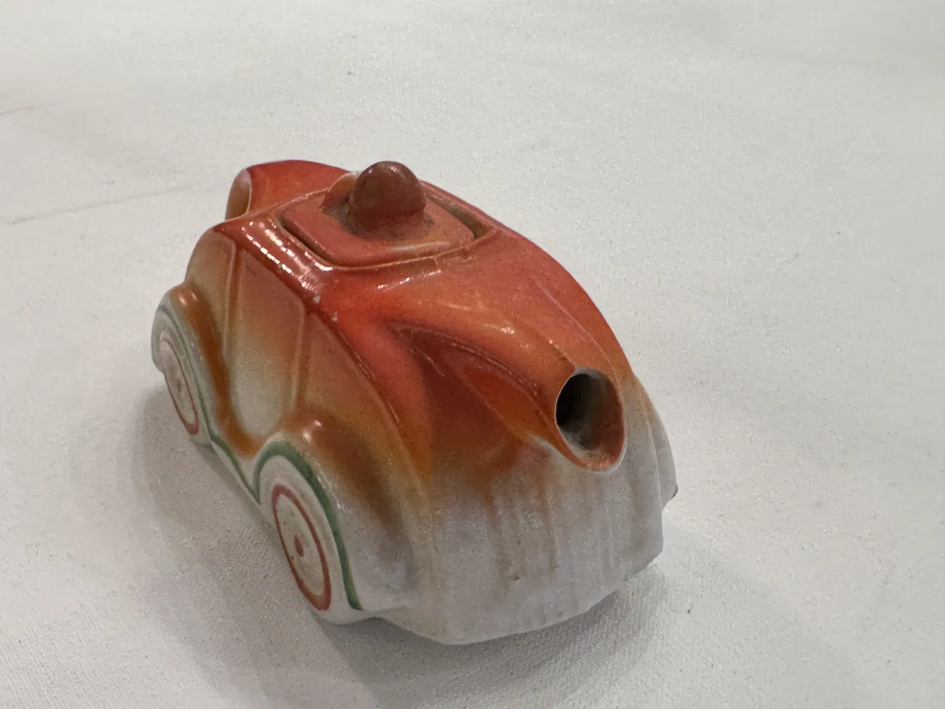 Peça de cerâmica antiga em forma de carro com cores vibrantes.