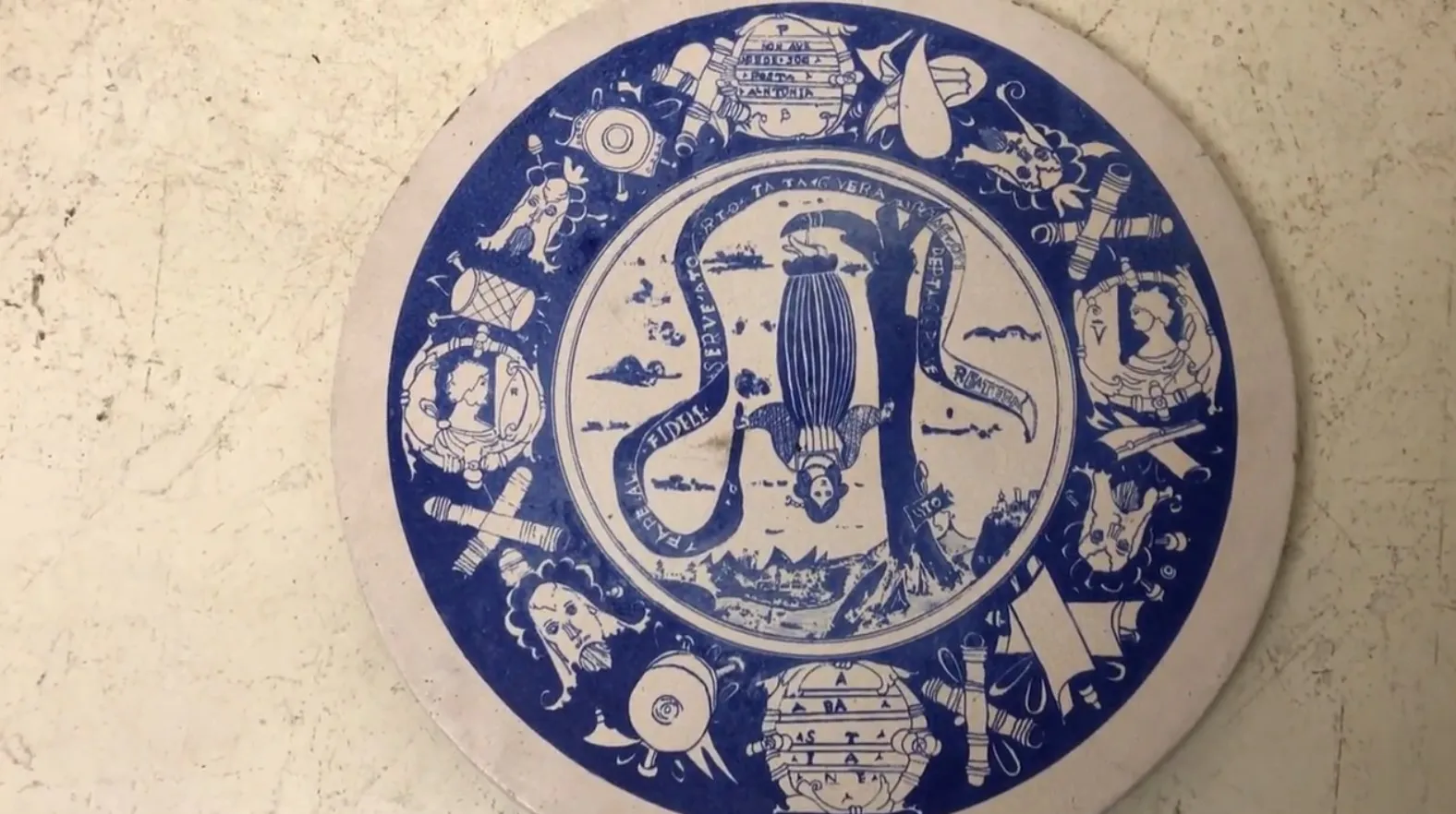 Prato de cerâmica decorado com ilustrações vintage em azul e branco, apresentando uma figura central com um fundo marinho.