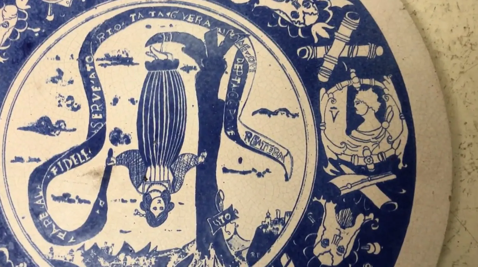 Prato antigo de cerâmica, pintado em azul e branco, decorado com figuras artísticas e detalhes cênicos.