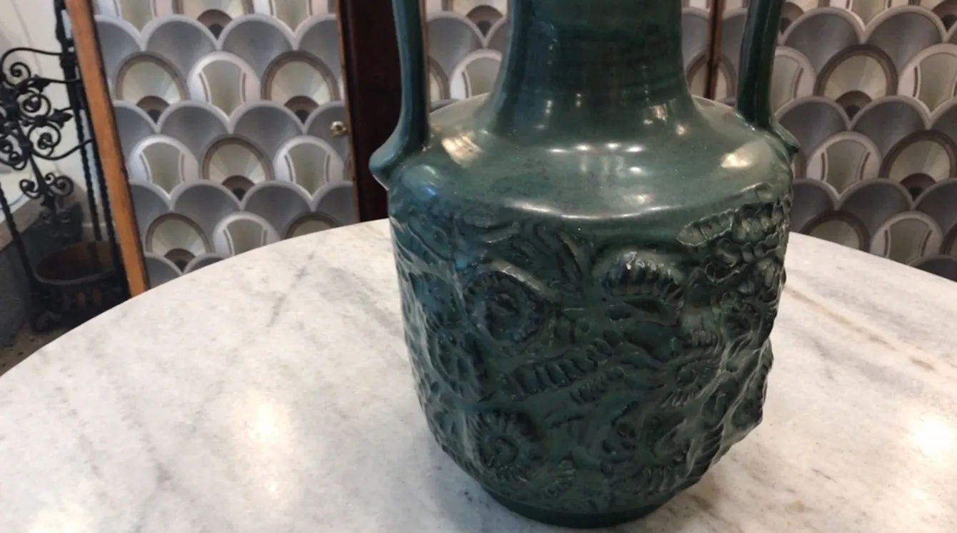 Carafe en céramique ancienne avec un design naturel en relief, sur une table en marbre.