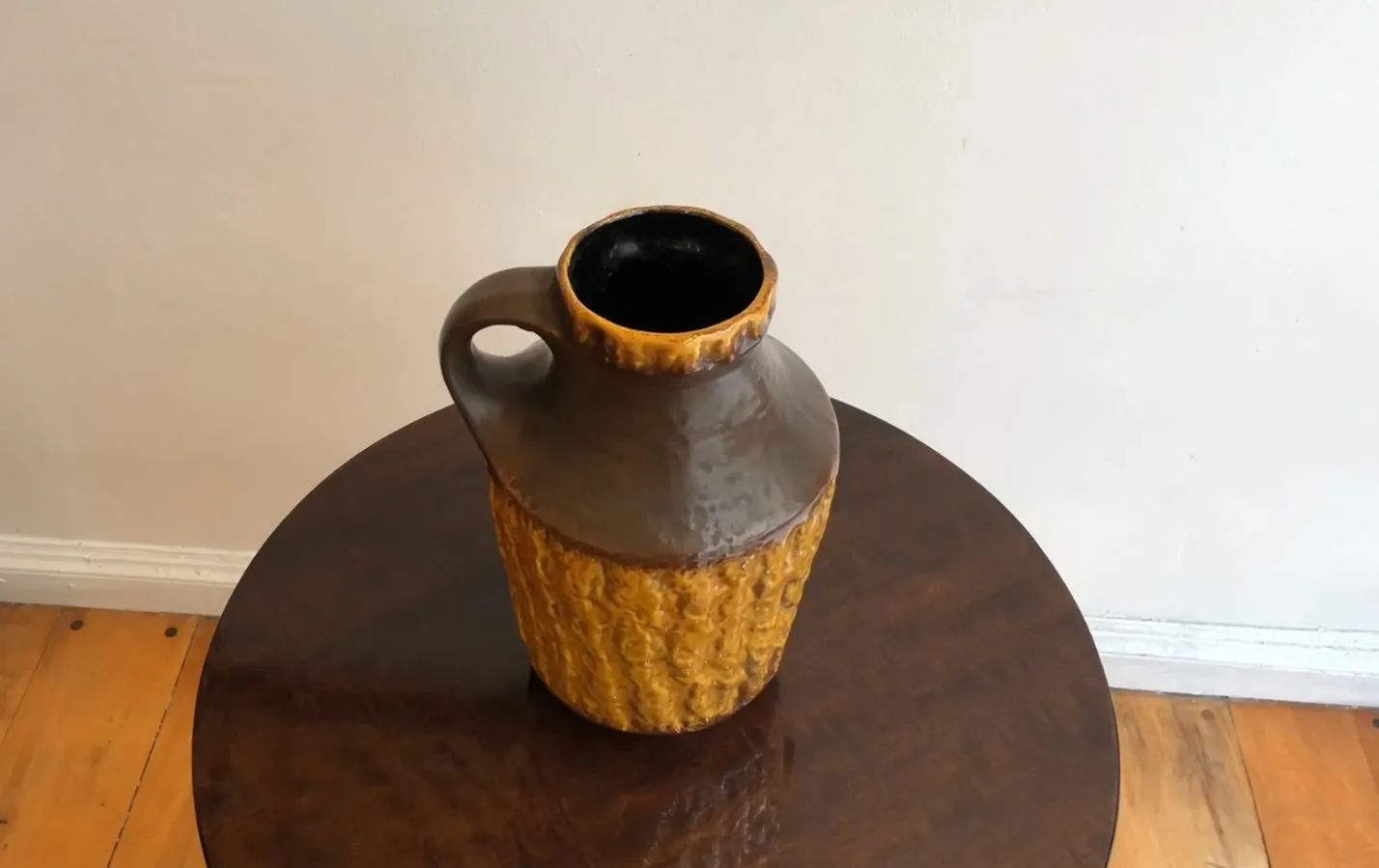 Giara di ceramica antica con texture nei toni marroni e gialli, presentata su un tavolo di legno.