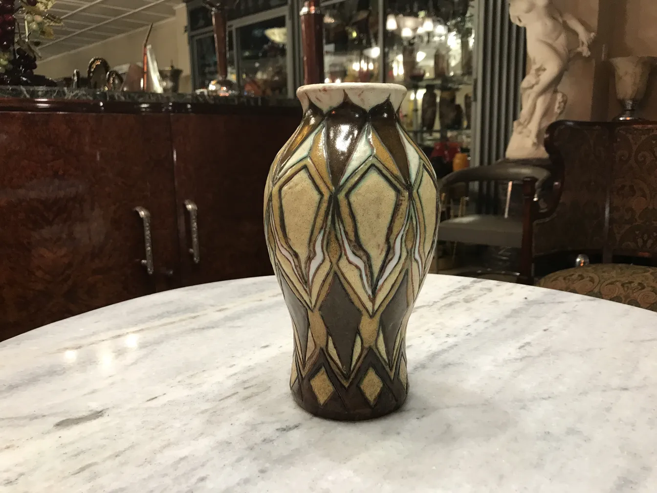 Vaso de cerâmica antiga com design decorativo em tons de bege e marrom, sobre uma mesa.