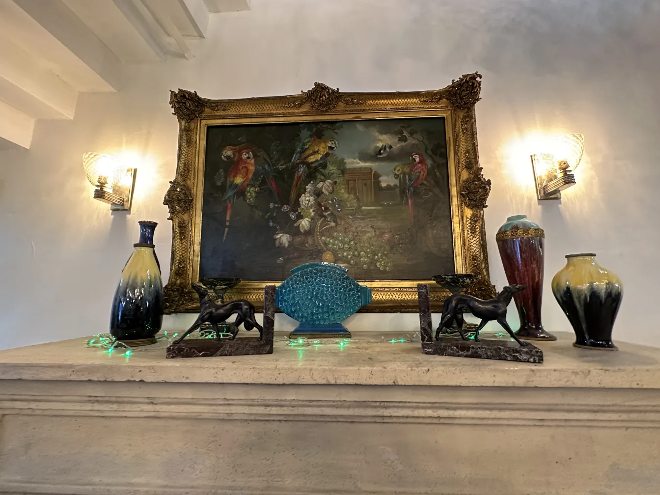Cerámica antigua variada en una repisa con objetos decorativos y un cuadro