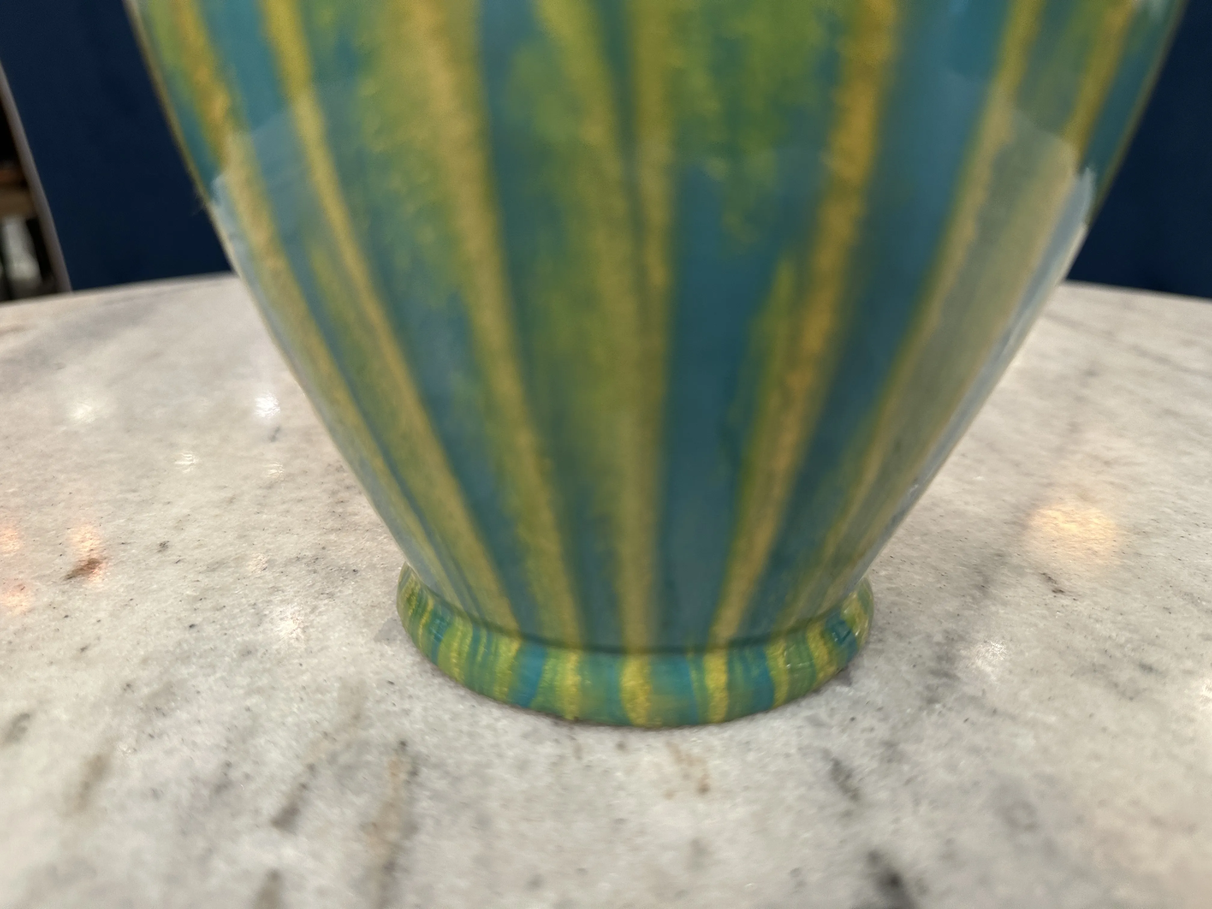 Antigua cerámica colorida con diseño en tono verde y amarillo sobre una base en una mesa.