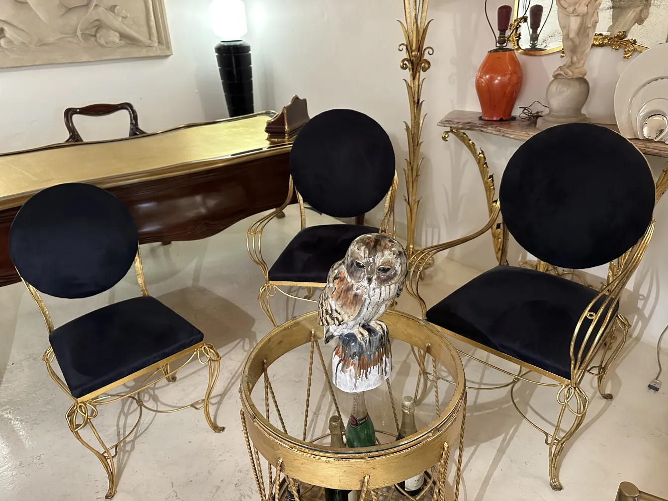 Três cadeiras antigas com almofadas pretas e uma coruja decorativa.