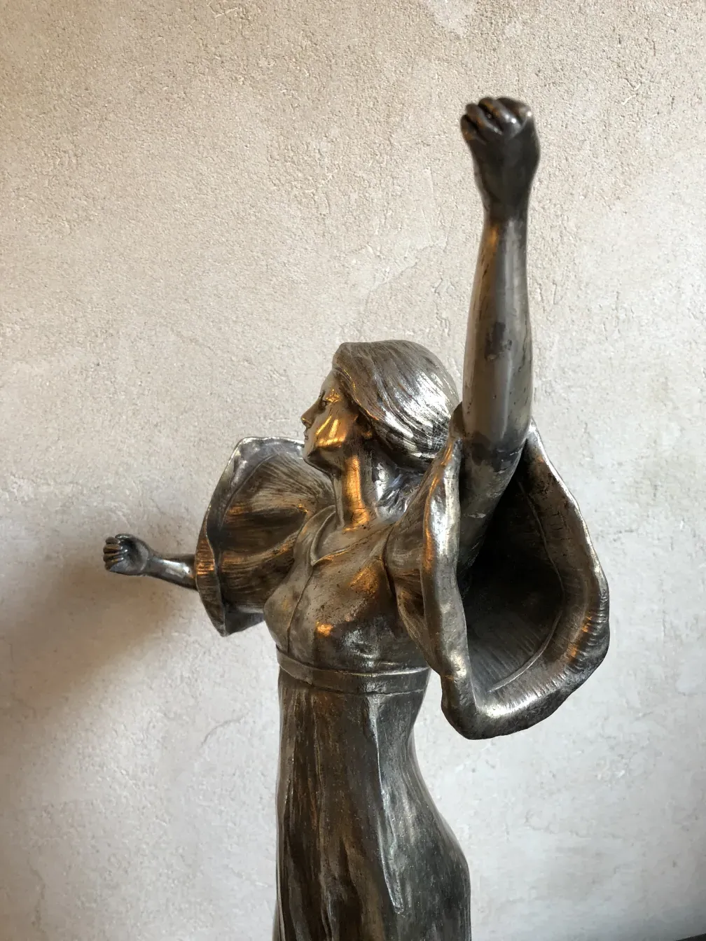escultura antigua en metal con brazos levantados