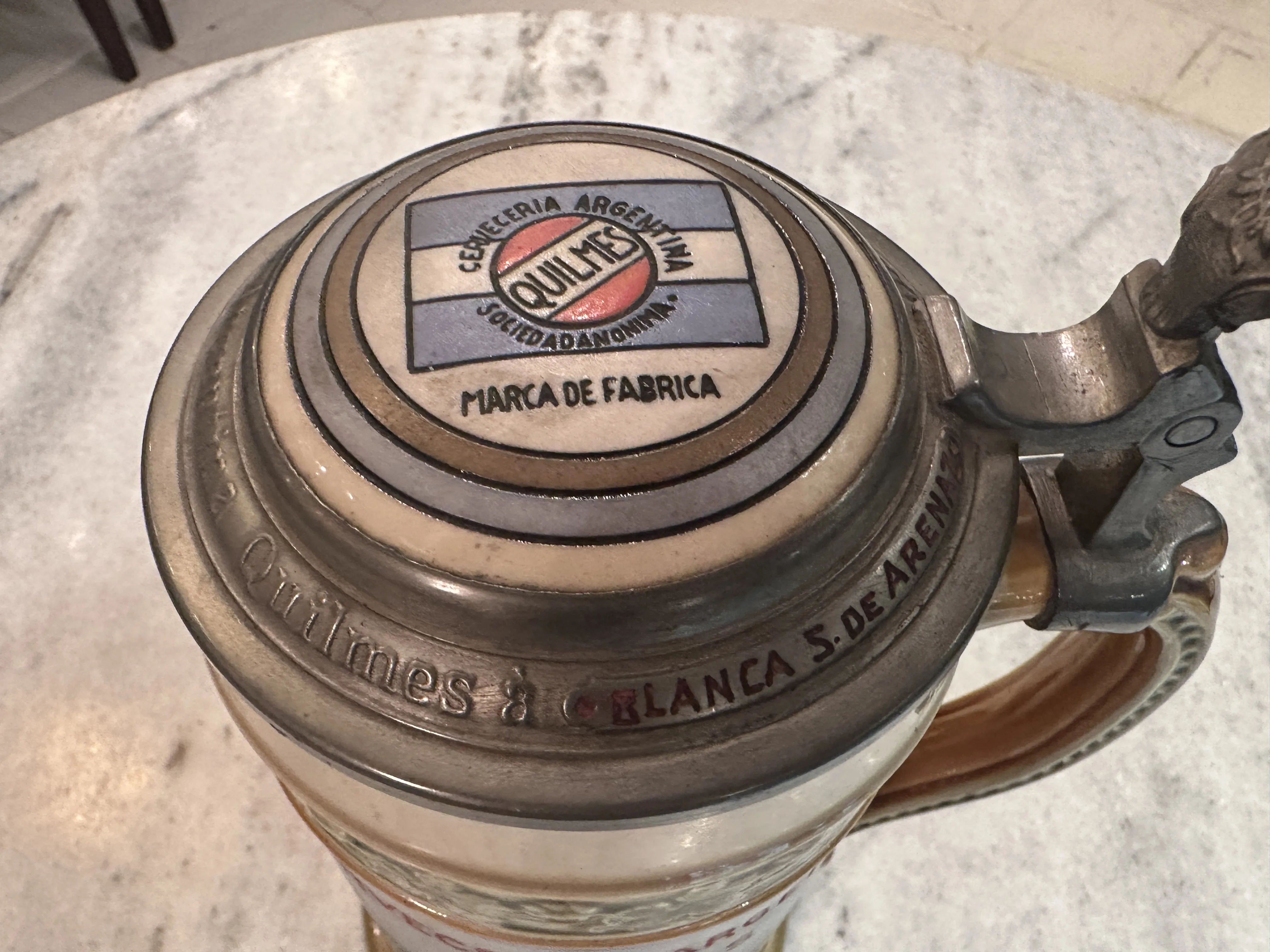Taza de cerámica antigua con marca 'Quilmes' en la tapa.