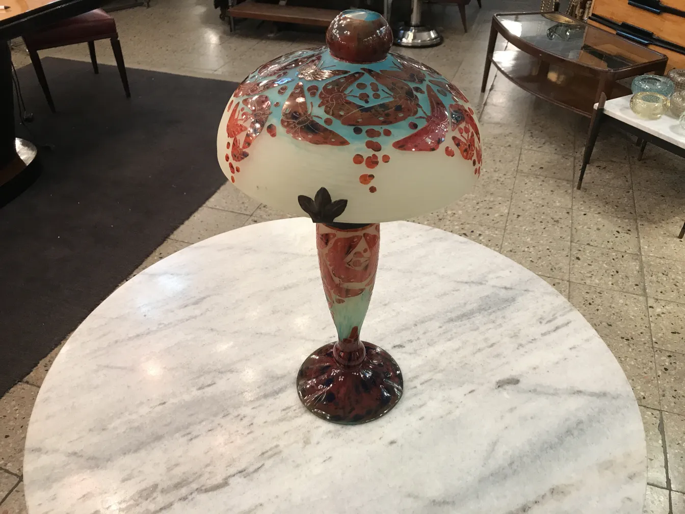 Lâmpada de vidro antigo com tons coloridos e padrões decorativos, em uma mesa de mármore.