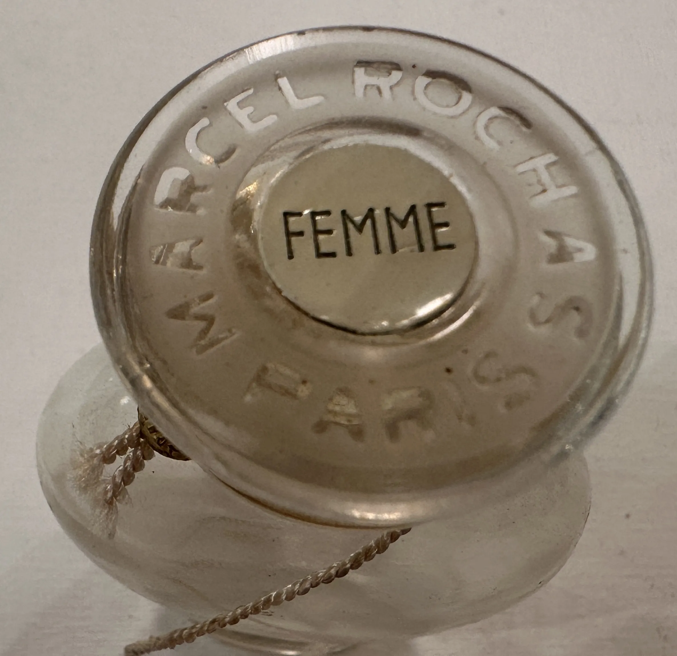 Frasco de perfume antigo de Marcel Rochas em cor clara com a palavra Femme na base.