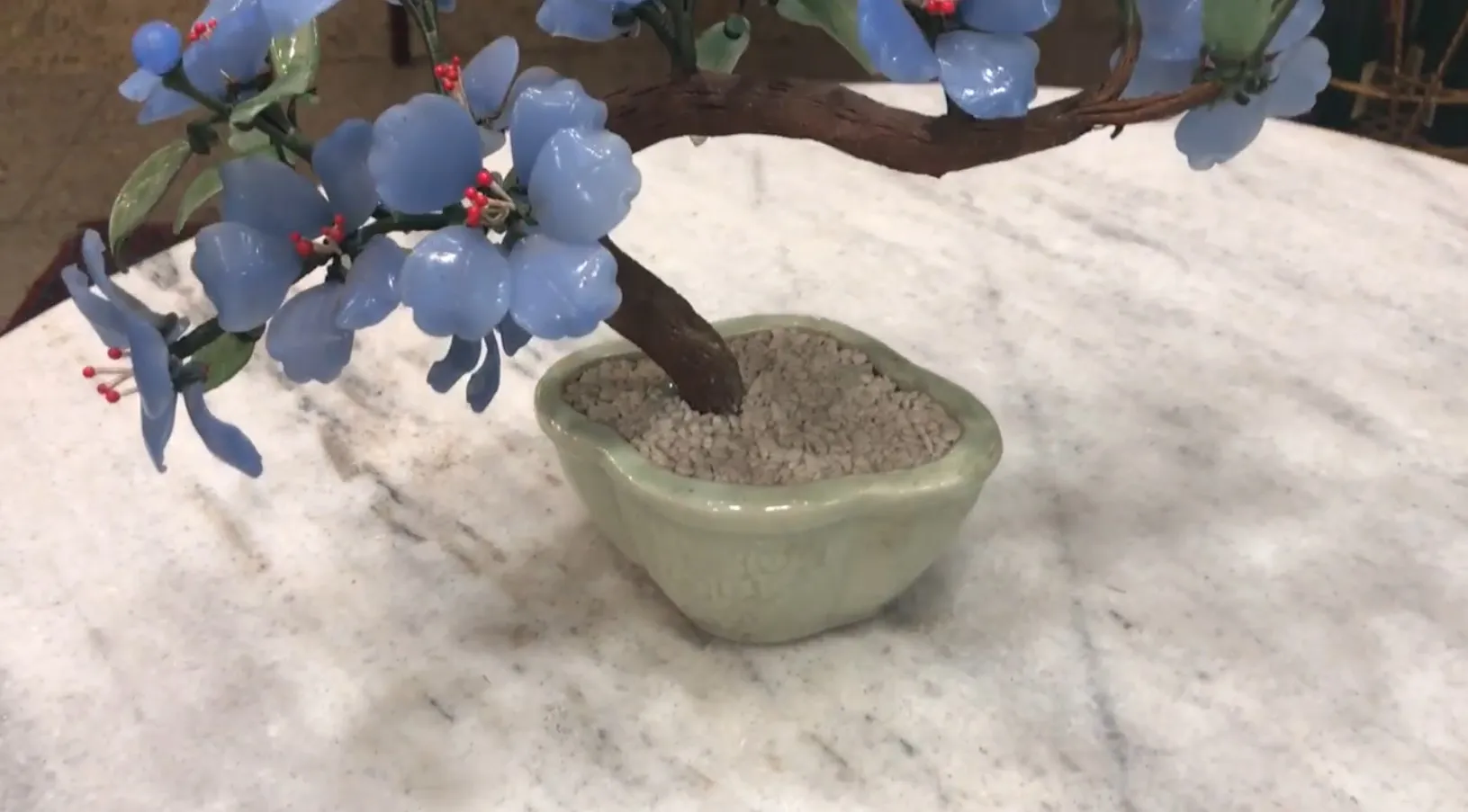 Bonsai antico con fiori blu in un vaso verde.