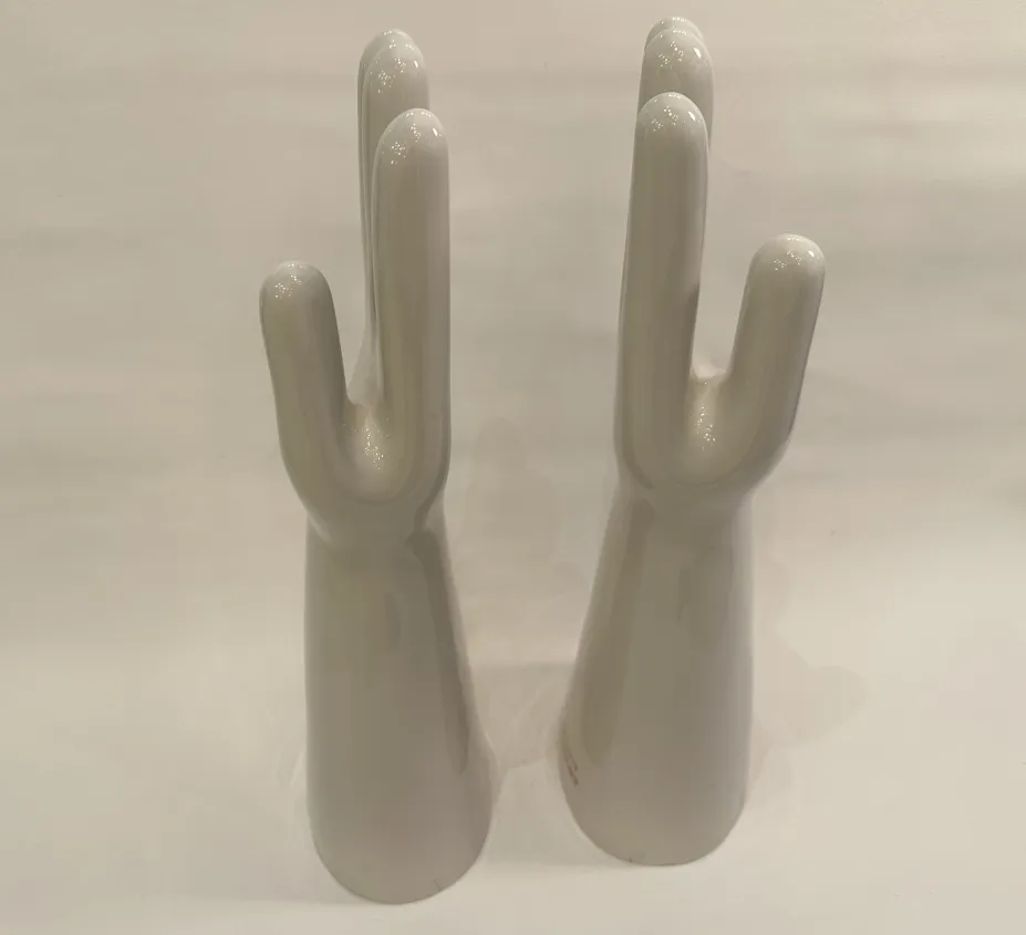 Coppia di mani in ceramica, antiche e lucide, con dettagli nella forma in uno sfondo neutro.