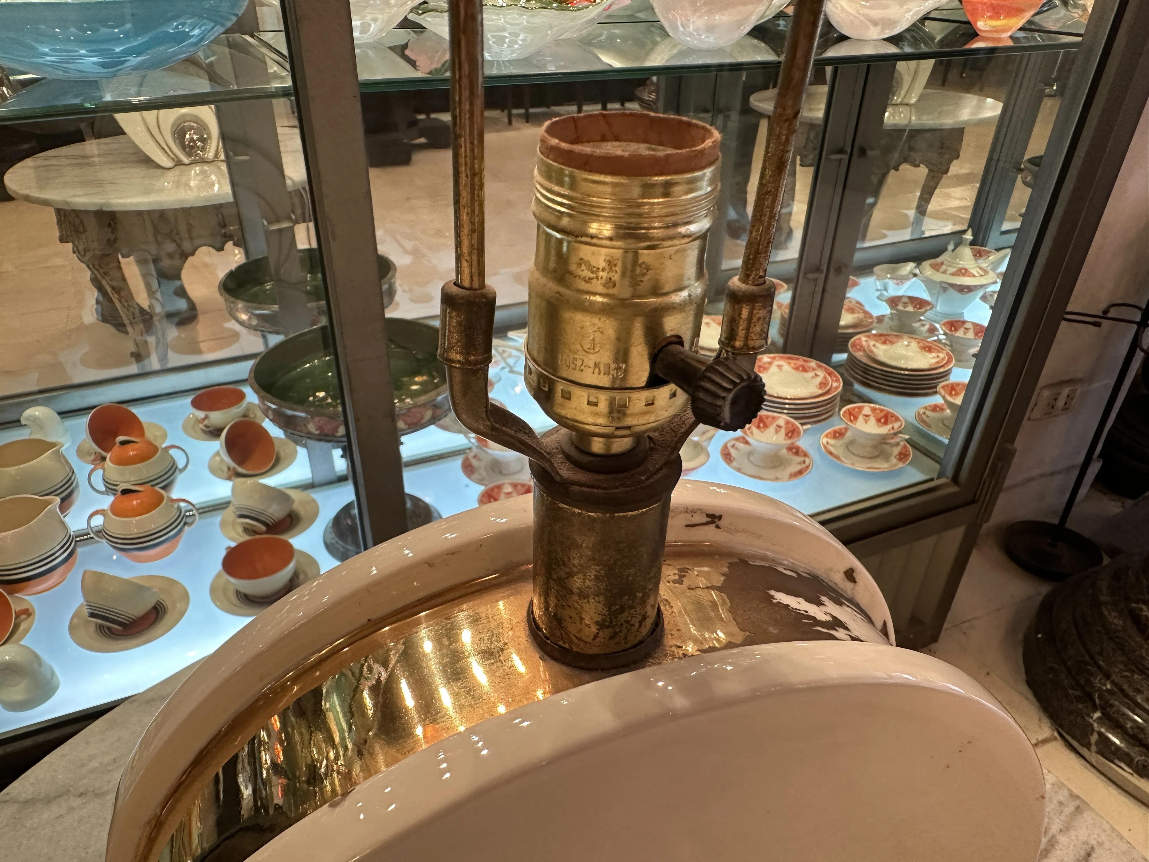 装飾的な古いテーブルランプ、丸いベースと金属のディテール。背景には皿とカップが展示されています。