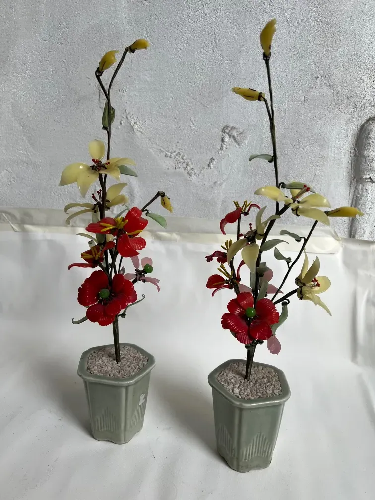 Dos bonsáis artesanales antiguos con flores rojas y amarillas en macetas verdes.