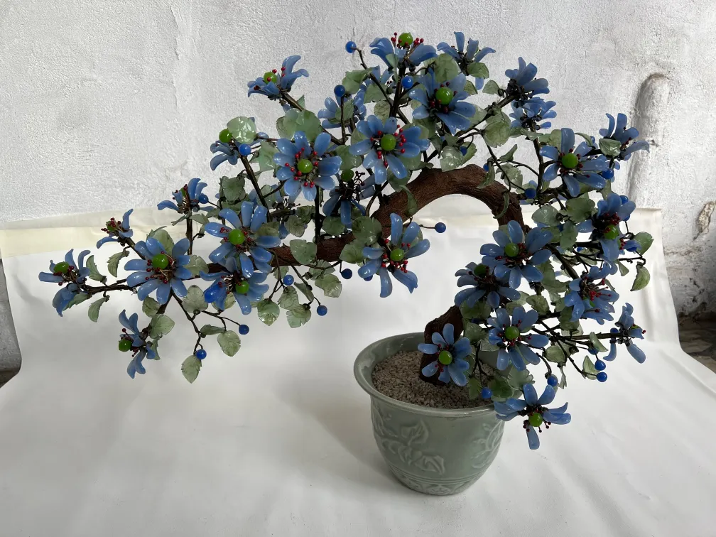 Antiker Bonsai mit blauen Blumen und dekorativen grünen Blättern.