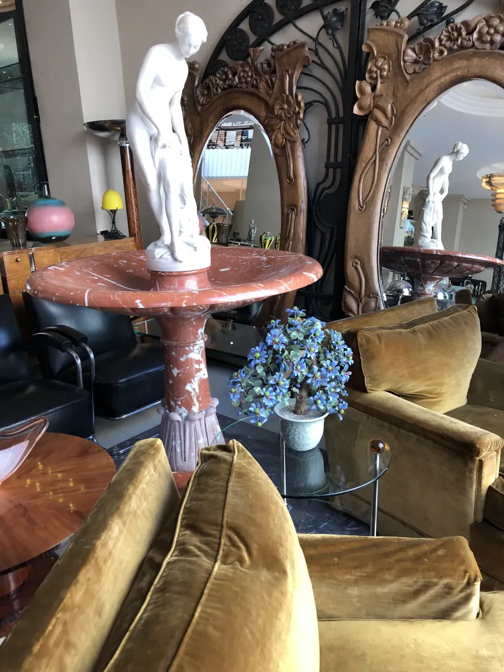 Bonsai antico su un tavolo circondato da poltrone verdi e una scultura.