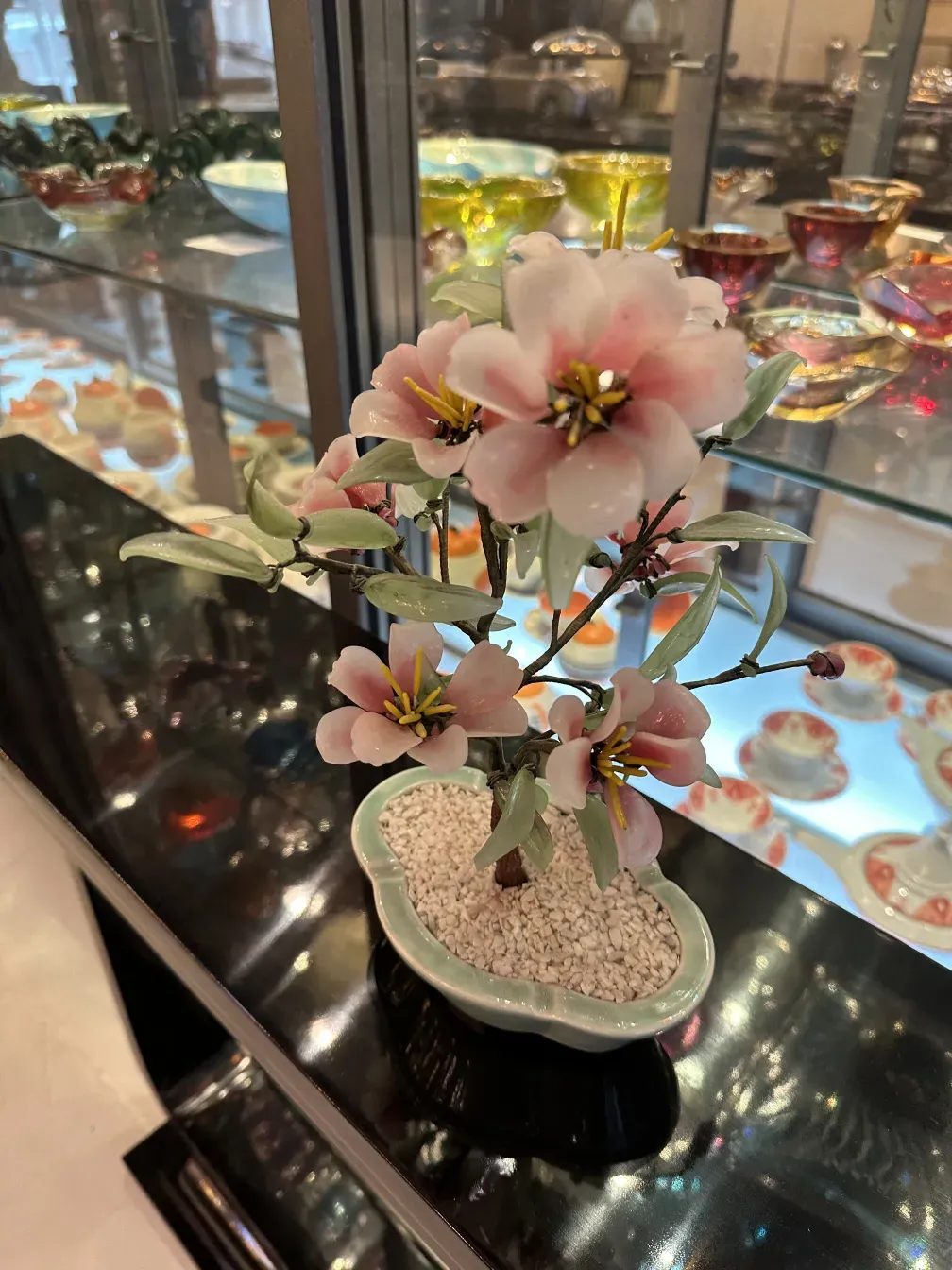 Bonsai antigo com flores rosas e folhas verdes em um vaso.