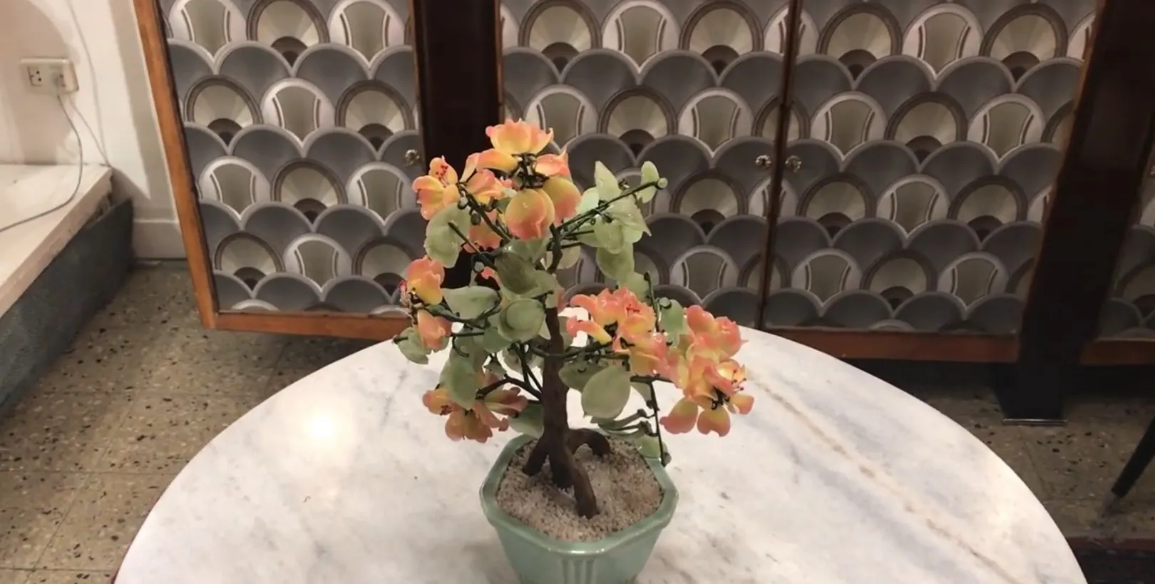 Antique bonsai planted in a green pot with pink flowers.