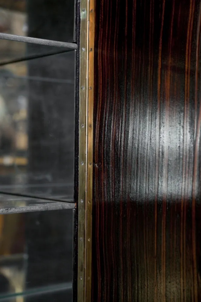 cabinete de bar antiquidade de gilbert poillerat com prateleiras transparentes em fundo escuro