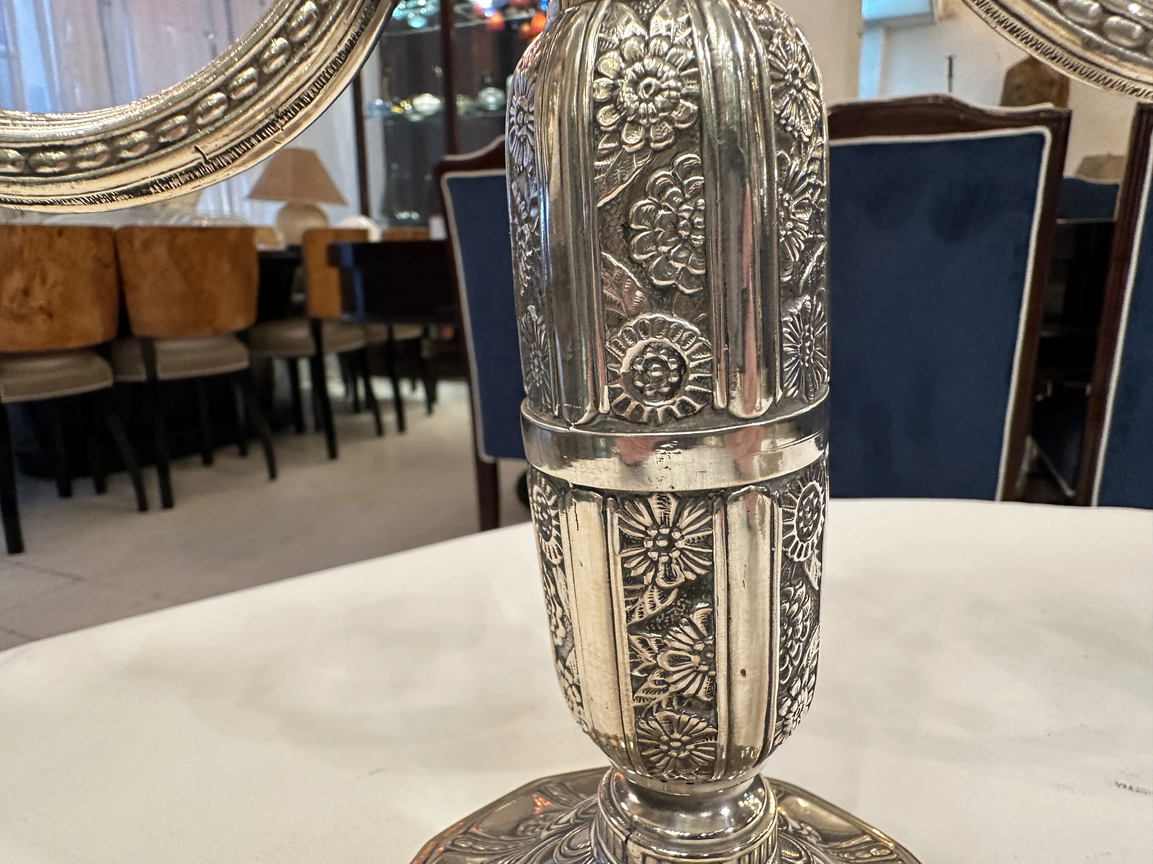 Dos candelabros antiguos con detalles en flor, situados sobre una mesa blanca, en un ambiente clásico y elegante.